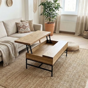May include: A wooden lift-top coffee table with a light brown finish and black metal legs. The table is open, revealing a storage compartment. The table is on a woven jute rug in a living room setting.