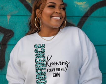 May include: A white long-sleeve sweatshirt featuring the text "CONFIDENCE" in a vertical orientation with a teal and black leopard print pattern, alongside the black text "Knowing I CAN'T BUT HE CAN" printed horizontally on the front.