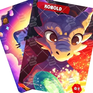 May include: Two fantasy art cards featuring a dragon and a creature with a cat-like face. The dragon card has the word "KOBOLD" in a red banner. The other card has a cat-like creature with a starry background. The cards have a rounded corner design.