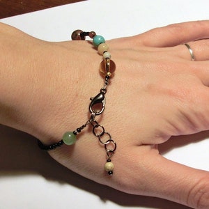 以下が含まれることがあります： 茶色、緑色、ターコイズ色のビーズ、銀色の留め具、銀色のチェーンエクステンションが付いたブレスレットです。