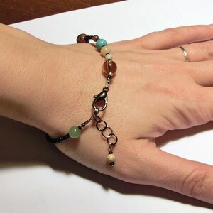 May include: A bracelet with brown, green, and turquoise beads, a silver clasp, and a silver chain extension.