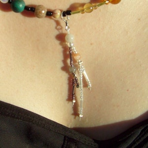 May include: A necklace featuring a mix of colourful beads, including green, brown, and yellow. A silver clasp connects the necklace to a dangling beaded pendant with clear and silver beads. The necklace is worn against a person's skin.