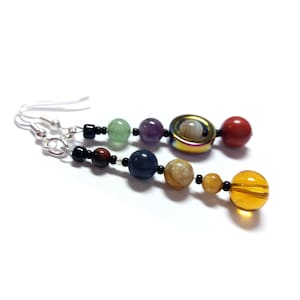May include: A pair of dangle earrings featuring a rainbow of gemstone beads, including green, purple, red, blue, and yellow. The earrings are crafted with black beads and silver fittings.