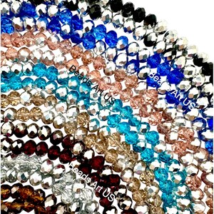May include: Assortment of faceted glass beads in various colors, including silver, black, blue, turquoise, brown, and pink. The beads are arranged in a semi-circle, with the text "Beads Art Us" visible on the bottom.