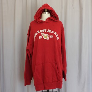 May include: Red hooded sweatshirt with a white graphic that says "Cole Boy Jeans Co. 19 77" with a small graphic of a plane in the middle.