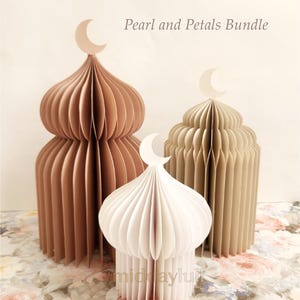 May include: Three honeycomb paper mosques in shades of muted pink, cream and white, resembling mosque domes, are arranged on a floral patterned surface. Each dome is topped with a crescent moon. The text "Pearl and Petals Bundle" is visible.