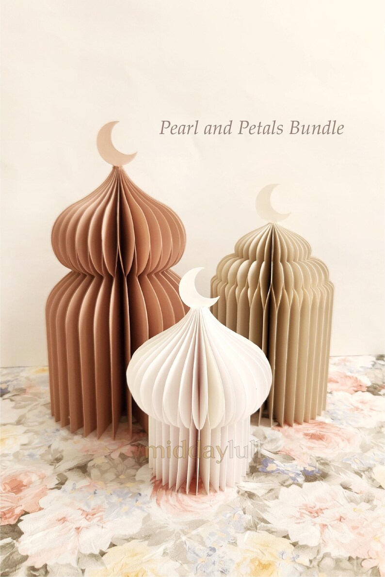 May include: Three honeycomb paper mosques in shades of muted pink, cream and white, resembling mosque domes, are arranged on a floral patterned surface. Each dome is topped with a crescent moon. The text "Pearl and Petals Bundle" is visible.