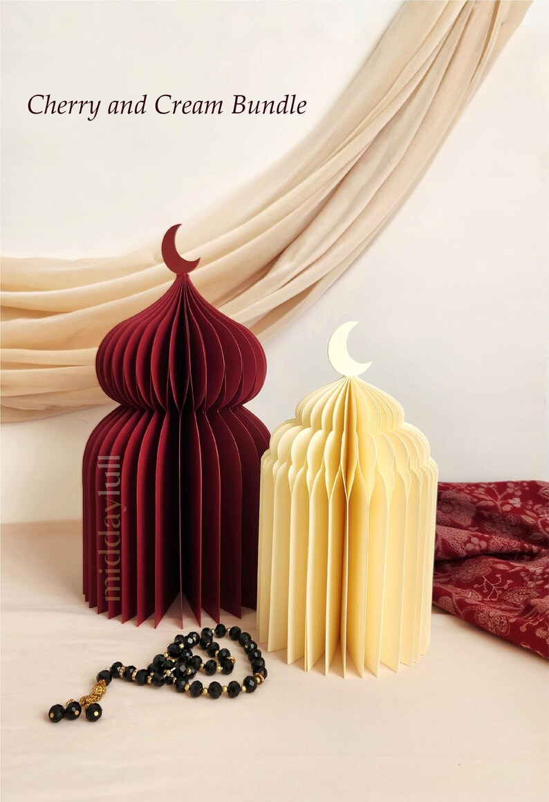 May include: Two paper mosque-shaped decorations, one cherry red and one cream, each topped with a crescent moon. A black prayer beads with gold accents lies in front. The text "Cherry and Cream Bundle" is at the top.