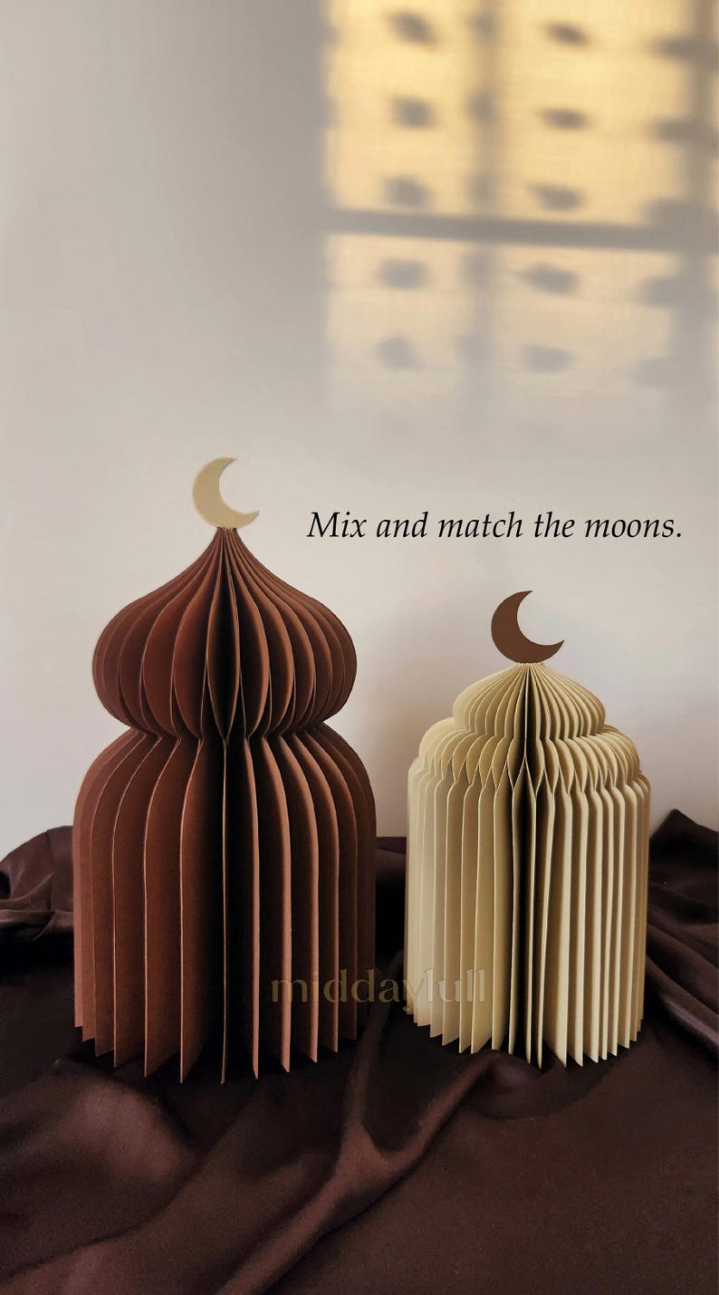 May include: Two paper dome-shaped decorations, one brown and one cream, each topped with a crescent moon. The brown dome has a light beige moon, and the cream dome has a dark brown moon. Text reads "Mix and match the moons."