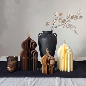 Set of three minimalist paper mosques in chocolate, tan, and cream colors topped with crescent moons, styled on a Ramadan tablescape with a black vase and dried eucalyptus."
