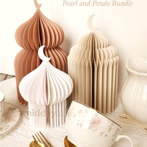 May include: A display of paper lanterns in white, beige, and brown, each with a crescent moon detail. A floral teacup, gold cutlery, and a white jug are also present. The text "Pearl and Petals Bundle" is visible in the image.