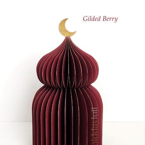 May include: A burgundy paper dome-shaped decoration with a gold crescent moon on top. The text "Gilded Berry" is visible. The paper structure is made of many vertical, curved panels.