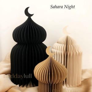 Three paper mosque-shaped decorations in varying sizes and colors: black, light brown, and cream. Each has a crescent moon on top. The text "Sahara Night" is visible.