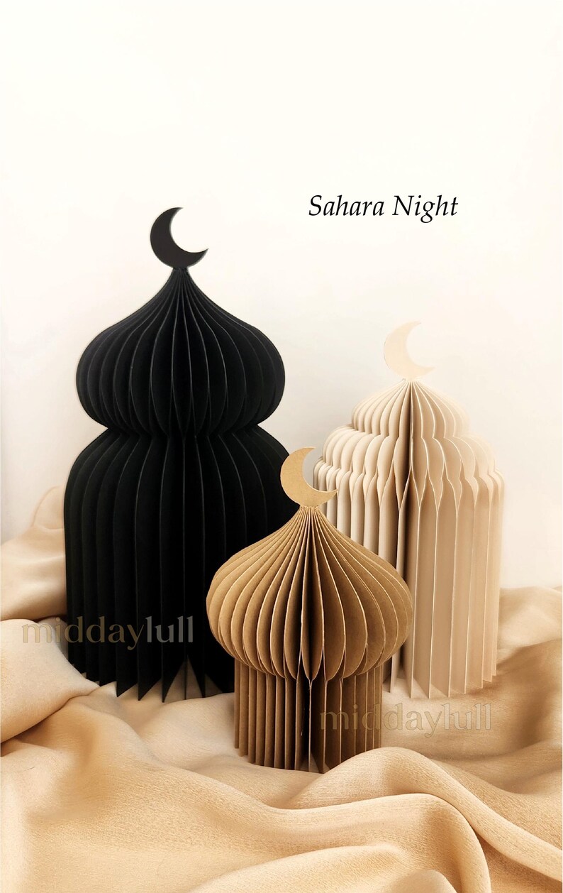 Three paper mosque-shaped decorations in varying sizes and colors: black, light brown, and cream. Each has a crescent moon on top. The text "Sahara Night" is visible.