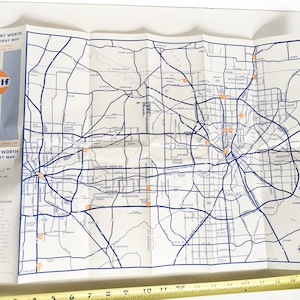 May include: A vintage Gulf Oil map of Dallas and Fort Worth, Texas. The map shows major highways and roads, with red dots marking Gulf gas stations. The map is folded and has a blue and orange Gulf logo in the bottom right corner.