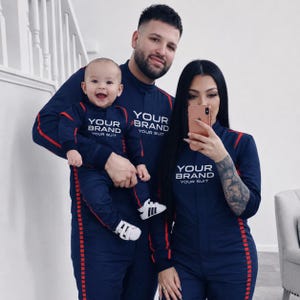 May include: Matching navy blue jumpsuits with red checkered side stripes and white text that reads YOUR BRAND YOUR SUIT. The jumpsuits feature a high collar, long sleeves, and a central zipper closure, designed for a coordinated family look.
