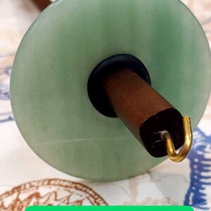 May include: Green aventurine spinning wheel whorl with a brown wooden spindle and a gold hook.