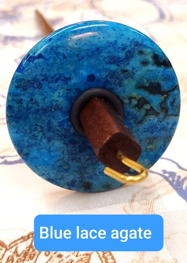 May include: A spinning wheel with a blue lace agate whorl, a dark brown wooden spindle, and a gold metal hook.