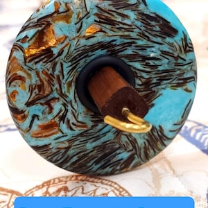May include: A turquoise and gold resin spinning wheel with a wooden spindle. The wheel has a swirling pattern of turquoise, gold, and black.
