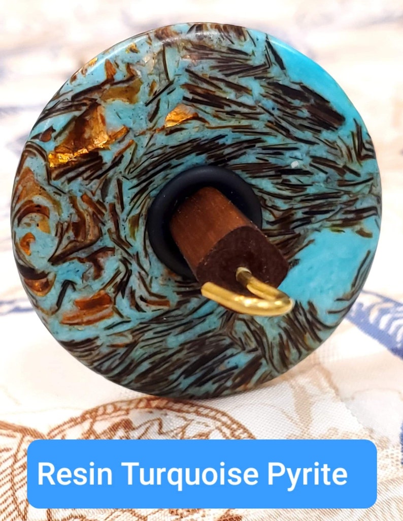May include: A turquoise and gold resin spinning wheel with a wooden spindle. The wheel has a swirling pattern of turquoise, gold, and black.