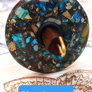 May include: A spinning wheel whorl made of blue jasper with a brown wooden spindle and a gold metal hook. The whorl has a speckled pattern of blue, brown, and white.