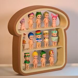 Puede incluir: Un estante de exhibición marrón en forma de pan que contiene doce pequeñas figuras desnudas con varios sombreros y accesorios. El estante tiene tres niveles y un interior beige claro, creando una solución de almacenamiento caprichosa y decorativa para coleccionables.