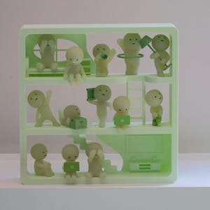 May include: A light green, multi-tiered shelf unit filled with small, off-white figurines. The figurines are in various poses, some holding objects like a flag or a box. The shelf unit has a minimalist design, with a staircase and a television.