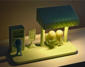 May include: A light green illuminated diorama lamp featuring a bus stop scene with a vending machine, a bus sign with Japanese text, and a shelter. Two figures sit on a bench under the shelter, while one figure stands by the vending machine.