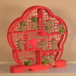 May include: A bright red decorative shelf with a lattice design, displaying several small figurines. The figurines are beige with red hats and some are holding accessories. A pink light bulb is in the centre of the shelf.