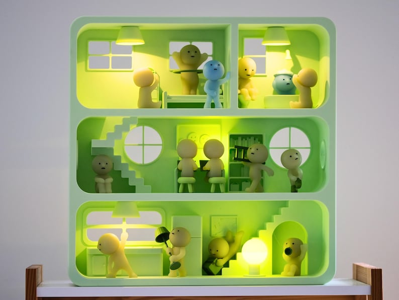 Puede incluir: Una estanter&iacute;a de exhibici&oacute;n en forma de casa de mu&ntilde;ecas de color verde claro con m&uacute;ltiples habitaciones, cada una con peque&ntilde;as figuras estilizadas. Las figuras est&aacute;n en varias poses, algunas interactuando con objetos. Las habitaciones est&aacute;n iluminadas con una luz c&aacute;lida y amarilla.