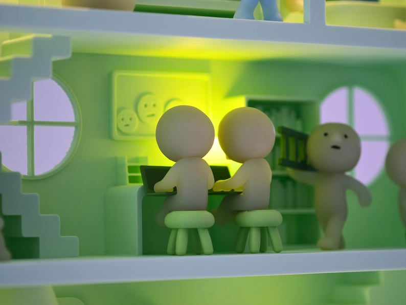 Puede incluir: Una escena de casa en miniatura caprichosa, de color verde claro, con varias figuras peque&ntilde;as de cabeza redonda. Dos figuras est&aacute;n sentadas en un escritorio con un port&aacute;til, mientras que otra lleva una peque&ntilde;a escalera. La escena incluye una escalera, una ventana y una pared con una imagen.
