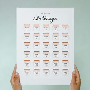 May include: A white canvas print with the words "NO SUGAR challenge" in black script. Below are 30 small jars labeled "Sugar" with numbers 1-30. The print is held by two hands against a light green background.