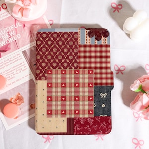 May include: A notebook cover with a patchwork design. It features red, cream, and navy blue patterns, including floral, plaid, and heart motifs. The cover has a layered aesthetic, with a variety of textures.