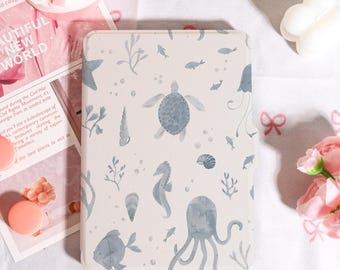 May include: A rectangular, off-white case with a watercolor-style sea life pattern. The design includes a turtle, seahorse, octopus, fish, and other marine elements in shades of gray. The case is surrounded by pink flowers and other decorative items.