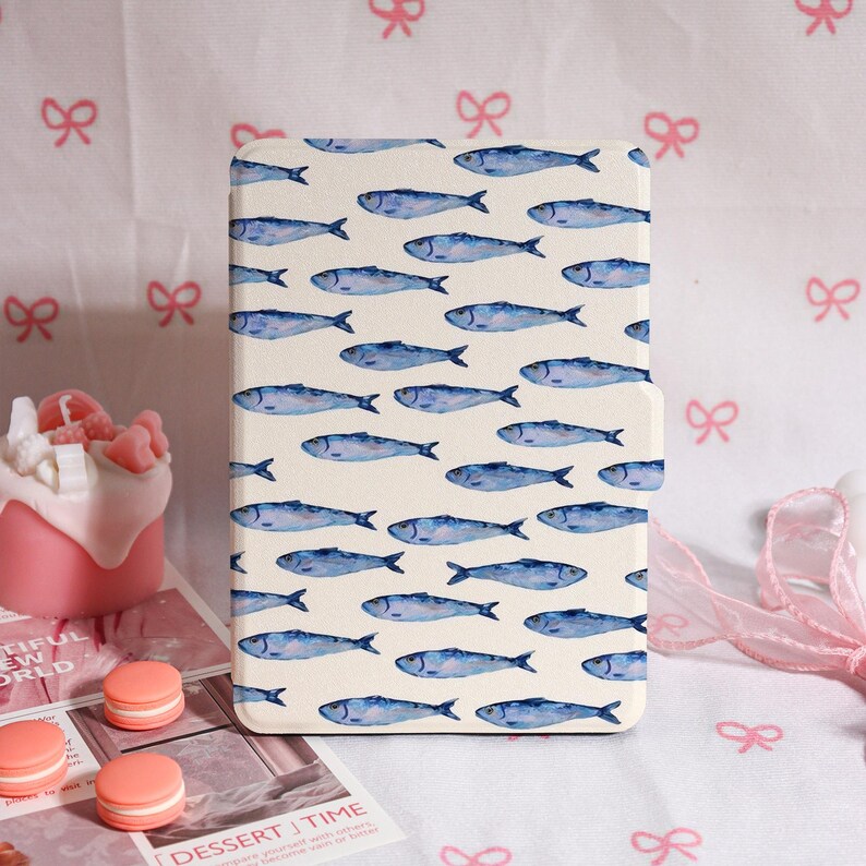May include: A cream-colored tablet case featuring a repeating pattern of blue fish. The case is rectangular and has a smooth finish. The design is reminiscent of watercolor illustrations, creating a whimsical and nautical theme.