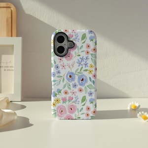 May include: A white phone case adorned with a floral design in shades of pink, blue, and yellow. The case has a camera aperture and a smooth surface. The pattern incorporates green leaves and stems, giving a spring-like appearance.