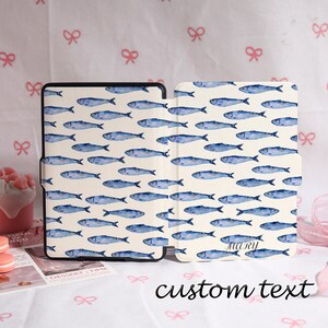 May include: A tablet case with a repeating pattern of blue watercolor fish on a cream background. The case is open, revealing the interior and exterior design. The text "custom text" is written in black script at the bottom.