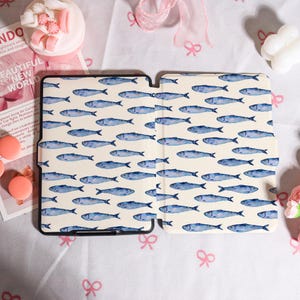 May include: A tablet case with a cream-colored background and a repeating pattern of blue watercolor fish. The case is open, revealing the interior. The text "BEAUTIFUL NEW WORLD" is visible in the background.