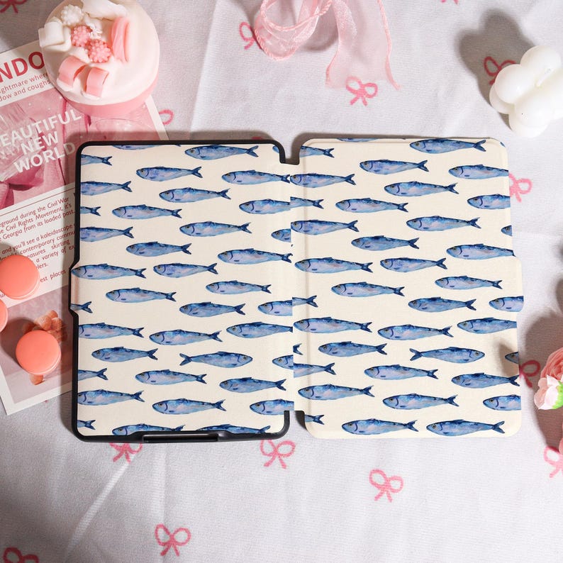 May include: A tablet case with a cream-colored background and a repeating pattern of blue watercolor fish. The case is open, revealing the interior. The text "BEAUTIFUL NEW WORLD" is visible in the background.