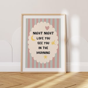 May include: A framed print with the words "NIGHT NIGHT LOVE YOU SEE YOU IN THE MORNING" in black text. The print has a light pink and blue striped background and a cream-colored oval with a heart, moon, and star design.