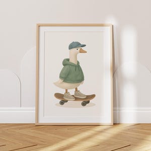 May include: A framed print showing a goose on a skateboard. The goose is depicted in a green hoodie, blue cap, and trainers. The skateboard is brown with black wheels. The artwork is set against a neutral background, framed in light wood, suitable for a child's room.