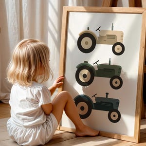 Little blonde girl admiring vintage tractor illustration art print in sunlit playroom, farm themed nursery wall decor with three tractors in neutral earth tones, beige green blue tractor poster for toddler boys room, rustic farmhouse kids bedroom artwork, vehicle transportation print children love, modern minimalist farm nursery aesthetic, large statement wall art in natural oak frame, country style children's room decoration, tractor loving toddler gift idea, warm golden light playroom styling.