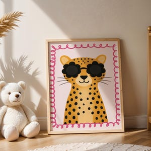 Adorable cheetah nursery art print with flower sunglasses displayed in baby room with teddy bear and wooden crib - cute leopard wall decor featuring pink scalloped border perfect for infant nursery design, newborn room decoration, baby girl bedroom art, safari animal themed nursery, wild cat illustration for children's spaces, nursery wall gallery, cozy baby room styling, modern nursery decor ideas, animal lover nursery theme, jungle inspired baby decor, wooden frame kids art.