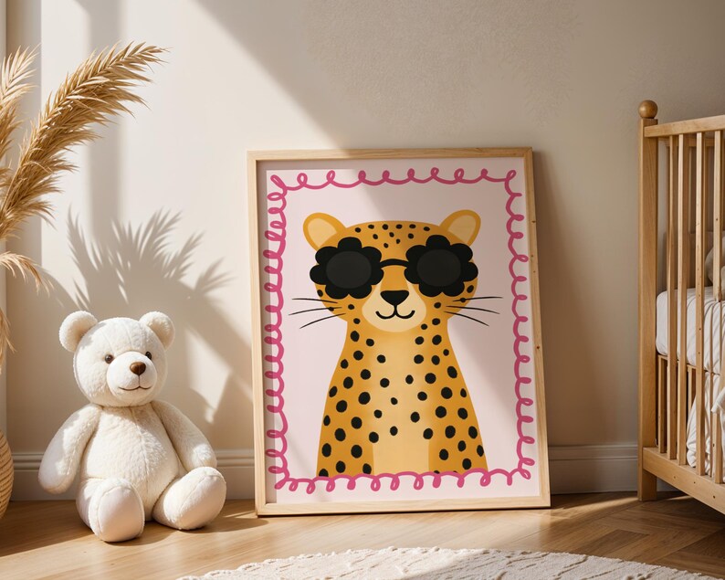 Adorable cheetah nursery art print with flower sunglasses displayed in baby room with teddy bear and wooden crib - cute leopard wall decor featuring pink scalloped border perfect for infant nursery design, newborn room decoration, baby girl bedroom art, safari animal themed nursery, wild cat illustration for children's spaces, nursery wall gallery, cozy baby room styling, modern nursery decor ideas, animal lover nursery theme, jungle inspired baby decor, wooden frame kids art.