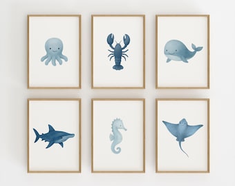 May include: Six framed watercolor prints featuring marine life. The prints depict an octopus, lobster, whale, shark, seahorse, and stingray in shades of blue. Each image is set against a white background and framed in light brown wood.