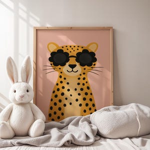 Cozy nursery decor with leopard wall art - spotted cheetah print with sunglasses in soft neutral nursery setting, wooden framed animal poster with white bunny plush toy, gentle nursery styling with cream blankets, calm baby room wall art, soft textures nursery design, peaceful children's bedroom decor, neutral toned animal themed nursery, comforting baby room artwork, serene nursery wall hanging, white and pink nursery color scheme, gentle safari animal print, soothing kids room poster.
