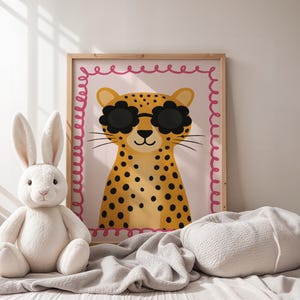 Adorable cheetah wall art with flower sunglasses in cozy nursery setting - cute leopard print with pink scalloped border perfect for baby room decor, neutral nursery design, soft textiles nursery, minimalist kids room art, Scandinavian style nursery, white bunny plush toys, gentle nursery styling, calm baby room atmosphere, natural light nursery, serene children's decor, peaceful nursery vibes, soft color palette kids art, hygge nursery design, comforting baby room.