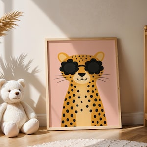 Leopard nursery wall art in baby room - cute spotted cheetah print with sunglasses next to crib, wooden framed animal poster for newborn nursery decor, safari themed baby room artwork, pink background jungle animal illustration, modern nursery wall hanging, boho baby room decor with pampas grass, teddy bear and leopard print nursery styling, contemporary children's animal art, baby shower gift idea, neutral nursery decor, crib room wall art, infant bedroom poster, stylish baby nursery prints.