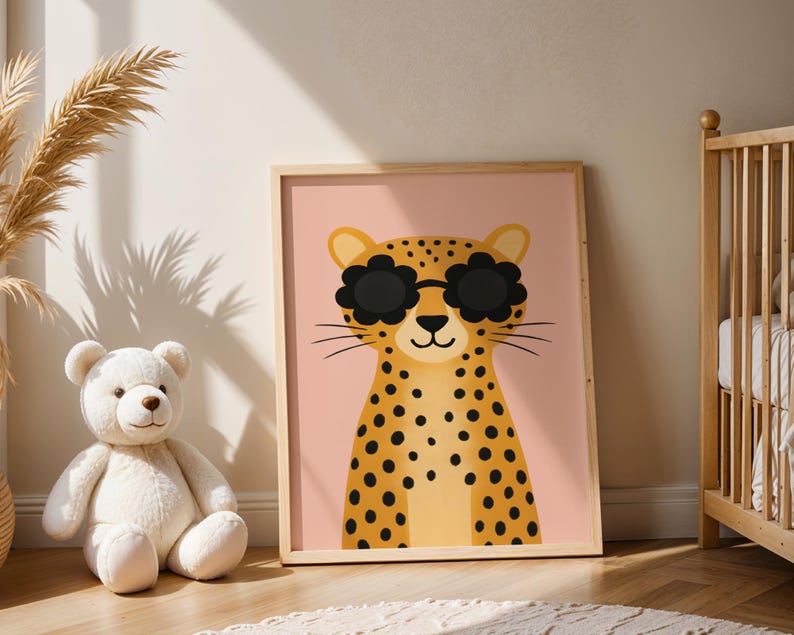 Leopard nursery wall art in baby room - cute spotted cheetah print with sunglasses next to crib, wooden framed animal poster for newborn nursery decor, safari themed baby room artwork, pink background jungle animal illustration, modern nursery wall hanging, boho baby room decor with pampas grass, teddy bear and leopard print nursery styling, contemporary children's animal art, baby shower gift idea, neutral nursery decor, crib room wall art, infant bedroom poster, stylish baby nursery prints.