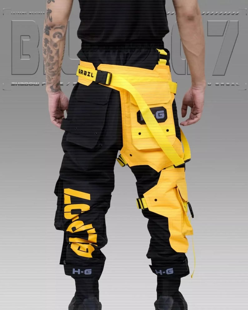 Puede incluir: Pantalones cargo negros y amarillos con m&uacute;ltiples bolsillos y correas. Los pantalones presentan detalles amarillos en las piernas y la cintura, con el texto "G7" impreso en amarillo en la pierna izquierda. El cintur&oacute;n de la cintura tiene el texto "GRAIL".